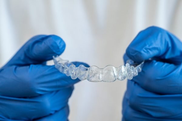Caucasian young man showing an invisible silicone aligner for dental correction. Male hand in gloves holding the plastic braces dentistry retainers to straighten teeth with white copy space.